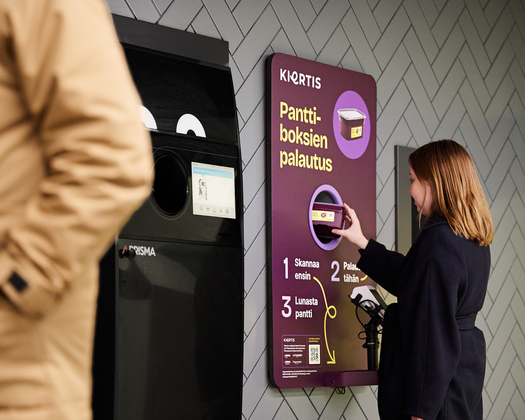 Henkilö näyttää miten uudelleenkäytettäviä takeaway-rasioita palautetaan Kiertis-palautusautomaattiin.